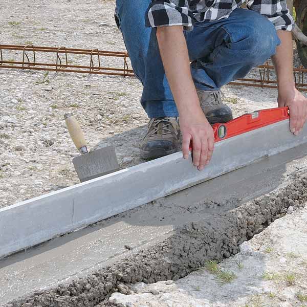 maçon en train de nivelé le béton avec une règle
